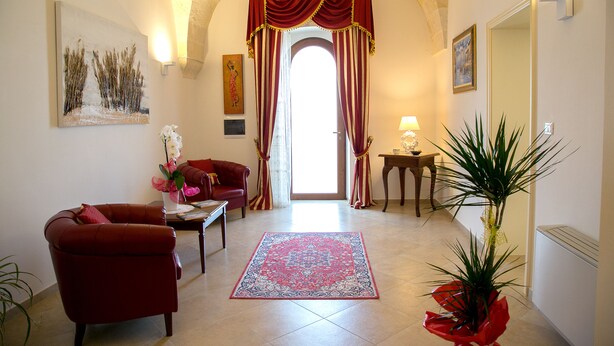 A living room with a red sofa, a coffee table, and a red rug. There is a door with red curtains and a painting on the wall. - B&B Monte Castello (Villa Castelli)