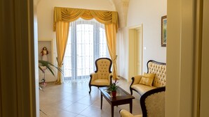 A spacious living room with high ceilings, a large arched window, and classic furniture. - B&B Monte Castello (Villa Castelli)