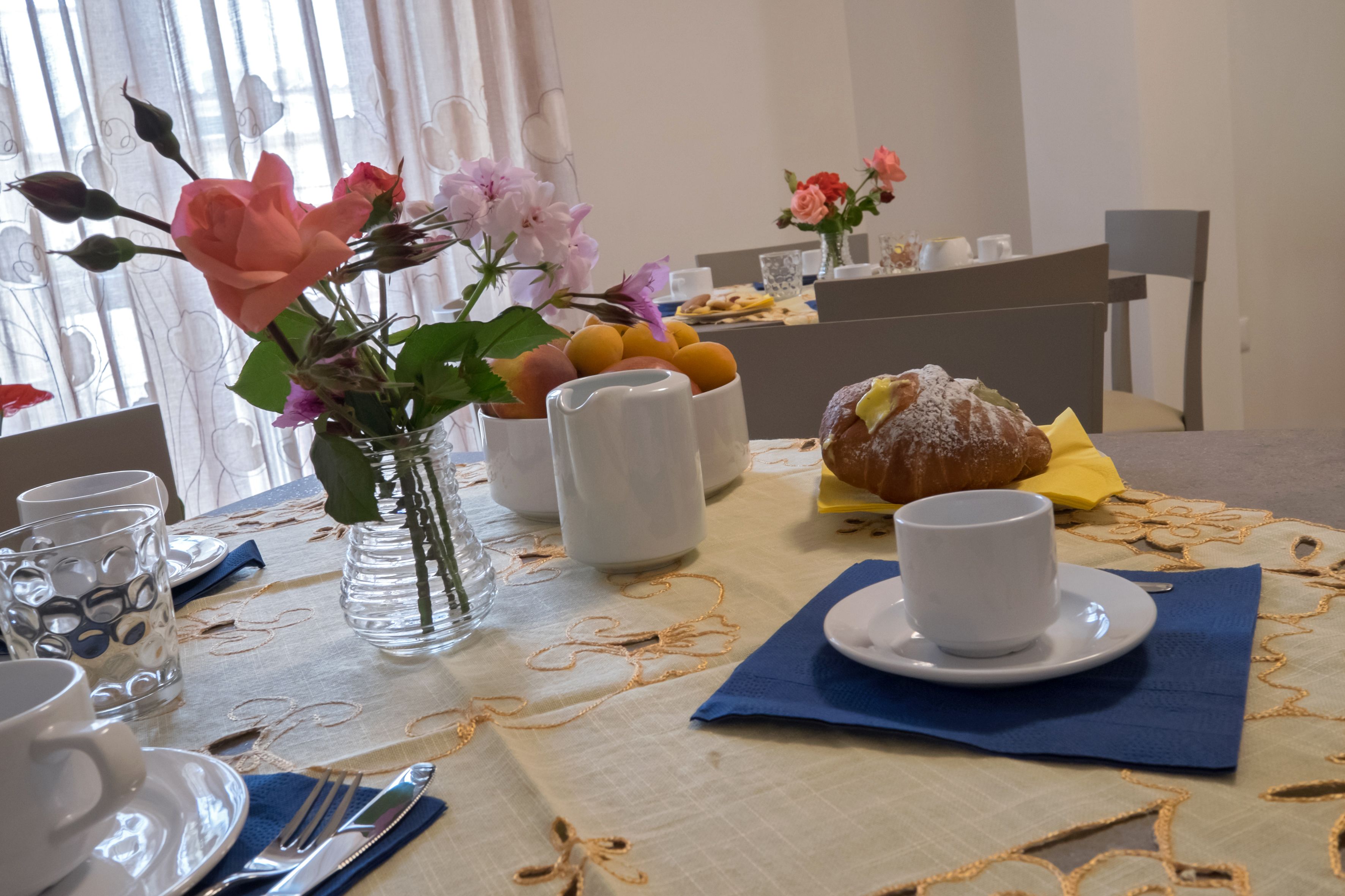 A dining table set with a vase of flowers, a croissant, and a cup.