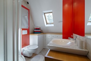 A modern bathroom with a skylight, a white toilet, a large sink, and a red accent wall.
