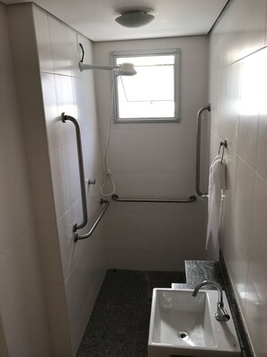 Une petite salle de bain étroite, avec une fenêtre, un lavabo et des barres d’appui.