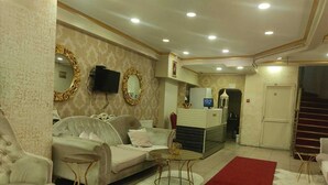 Un salon bien éclairé, avec un canapé, deux tables d’appoint, une moquette rouge et un comptoir de réception équipé d’un écran d’ordinateur.