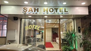 L’entrée de l’hôtel Sah se distingue par une porte en verre, un tapis rouge et des plantes en pot disposées à l’extérieur.