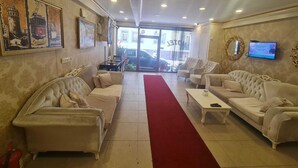Un hall d’hôtel avec deux canapés, une moquette rouge, un téléviseur et un tableau encadré au mur.