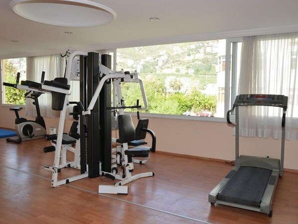 A gym with exercise equipment, a treadmill, and large windows with a view of greenery.