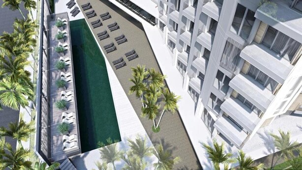 A modern hotel with a rooftop pool, sun loungers, and palm trees.