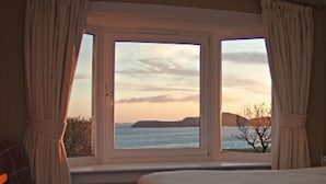 A room with a large window offering a view of the sea and distant land during sunset. - Summer Isles Hotel (Ullapool)
