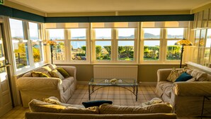 A sunlit room with two sofas, a coffee table, and large windows offering a view of greenery and hills. - Summer Isles Hotel (Ullapool)