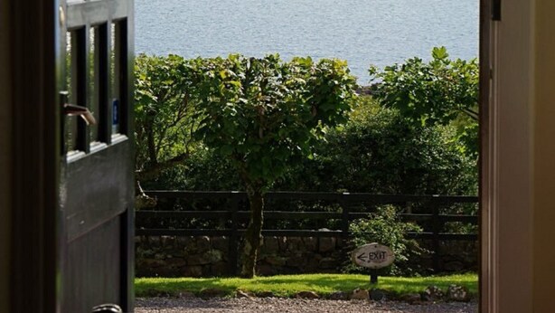 A view from a room with a door leading to a balcony overlooking a body of water and distant hills. - Summer Isles Hotel (Ullapool)