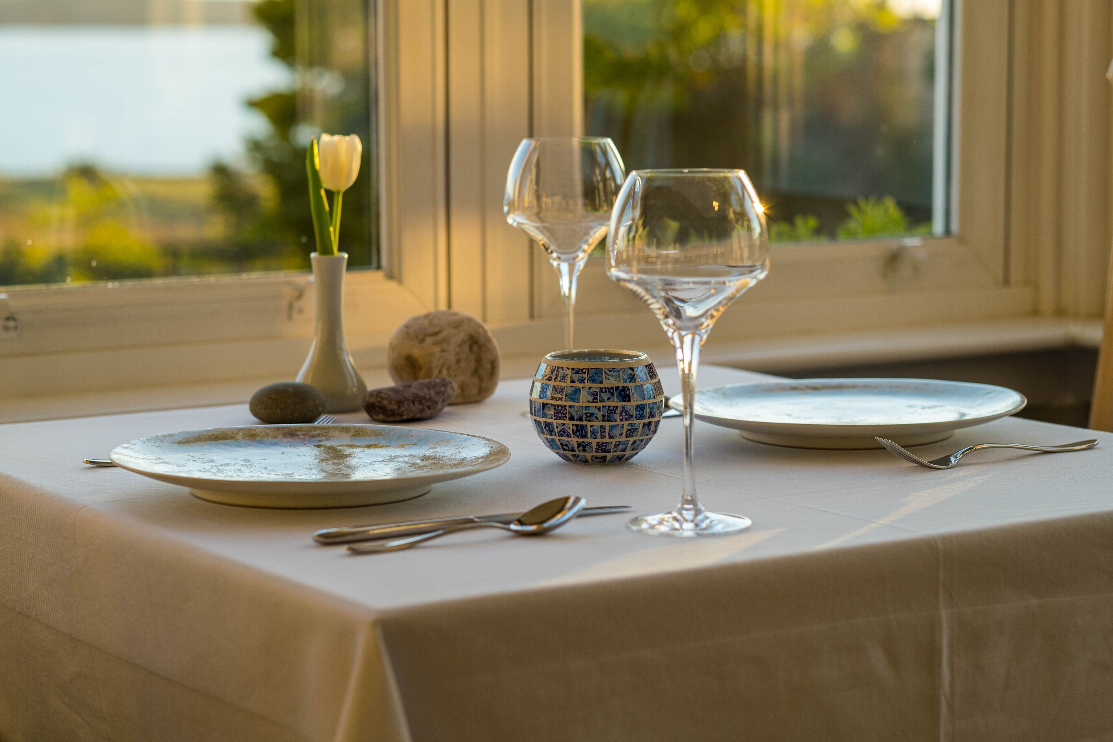 A table set with plates, a vase with a flower, a decorative bowl, and two wine glasses.