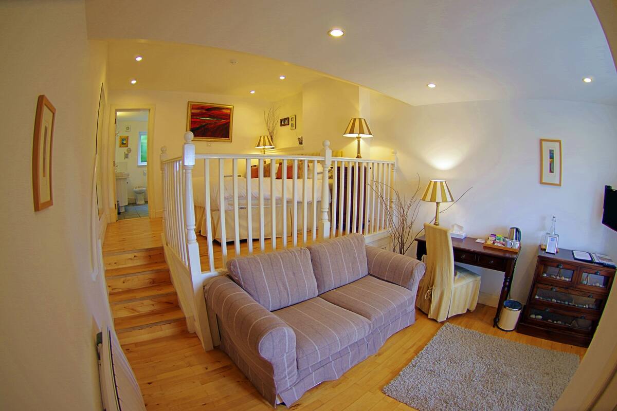 A cozy living room with a sofa, a desk, and a staircase leading to an upper floor.