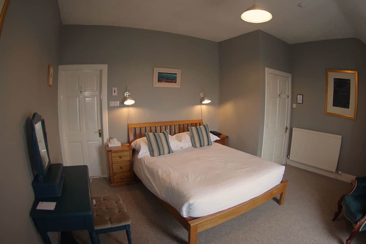A bedroom with a wooden bed, bedside tables, a dresser, a mirror, and a radiator.
