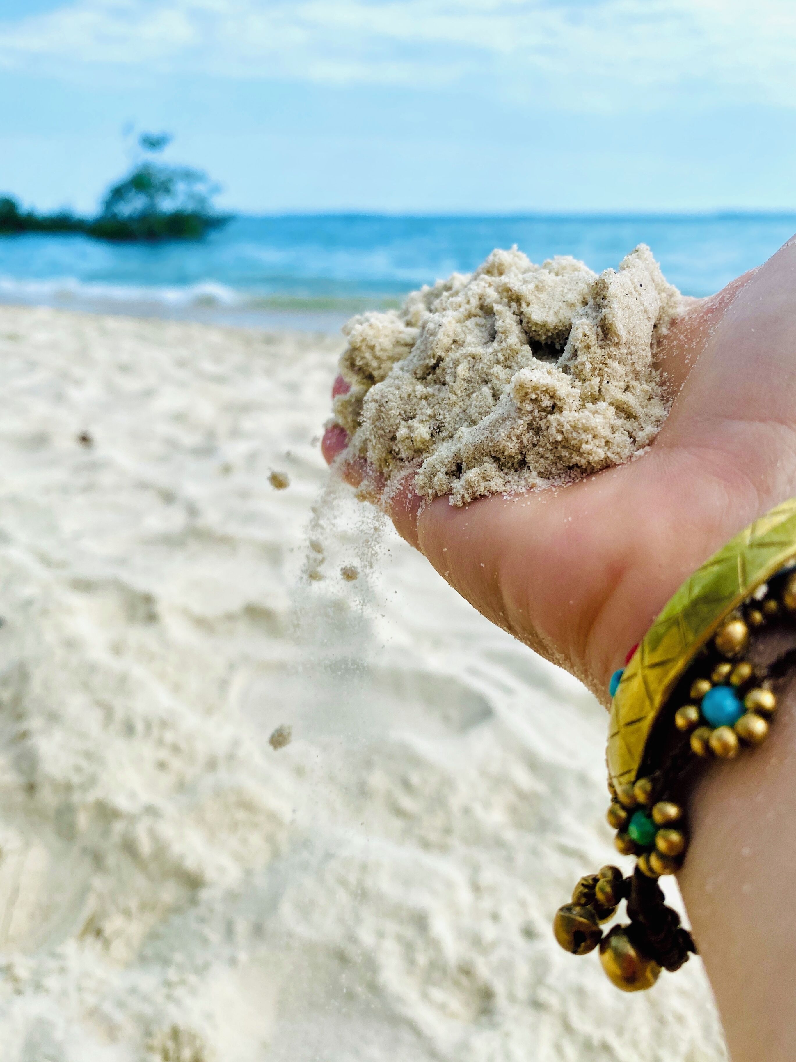 A hand holding sand with a beach and ocean in the background.