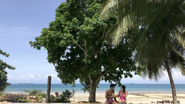 Una pareja sentada junto a una piscina con vistas a la playa y el océano.