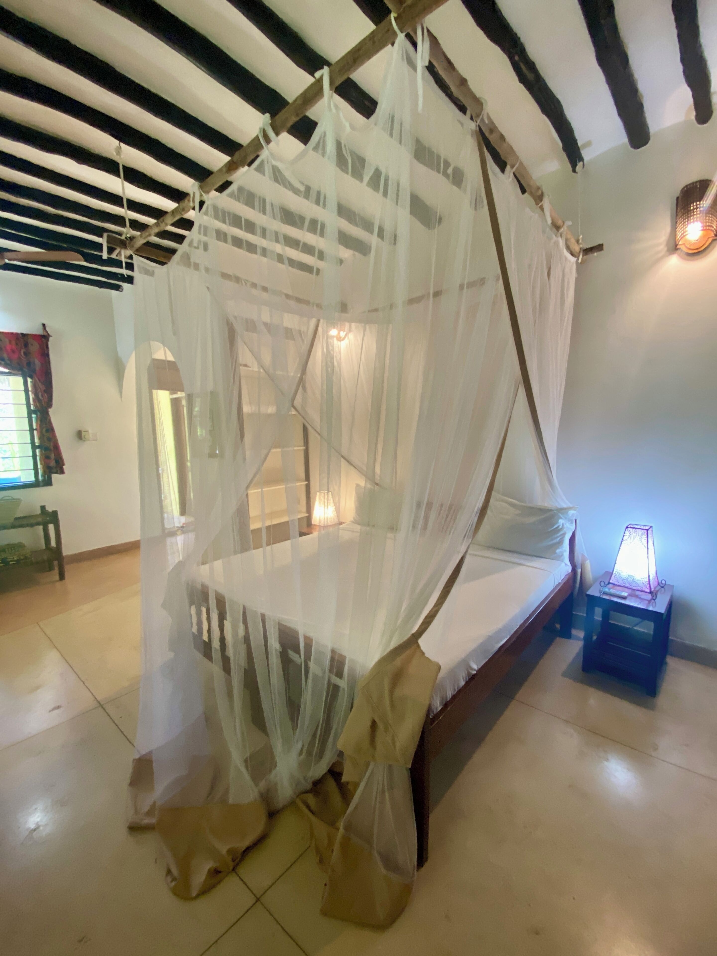 A room with a bed under a canopy, a nightstand with a lamp, and a wooden bench.
