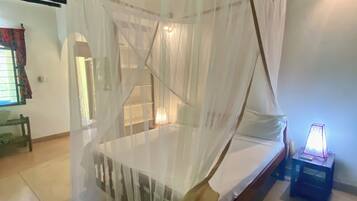 A room with a bed under a canopy, a nightstand with a lamp, and a wooden bench.