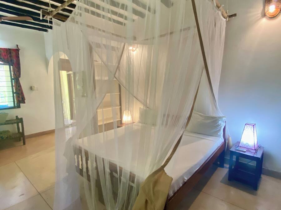 A room with a bed under a canopy, a nightstand with a lamp, and a wooden bench.