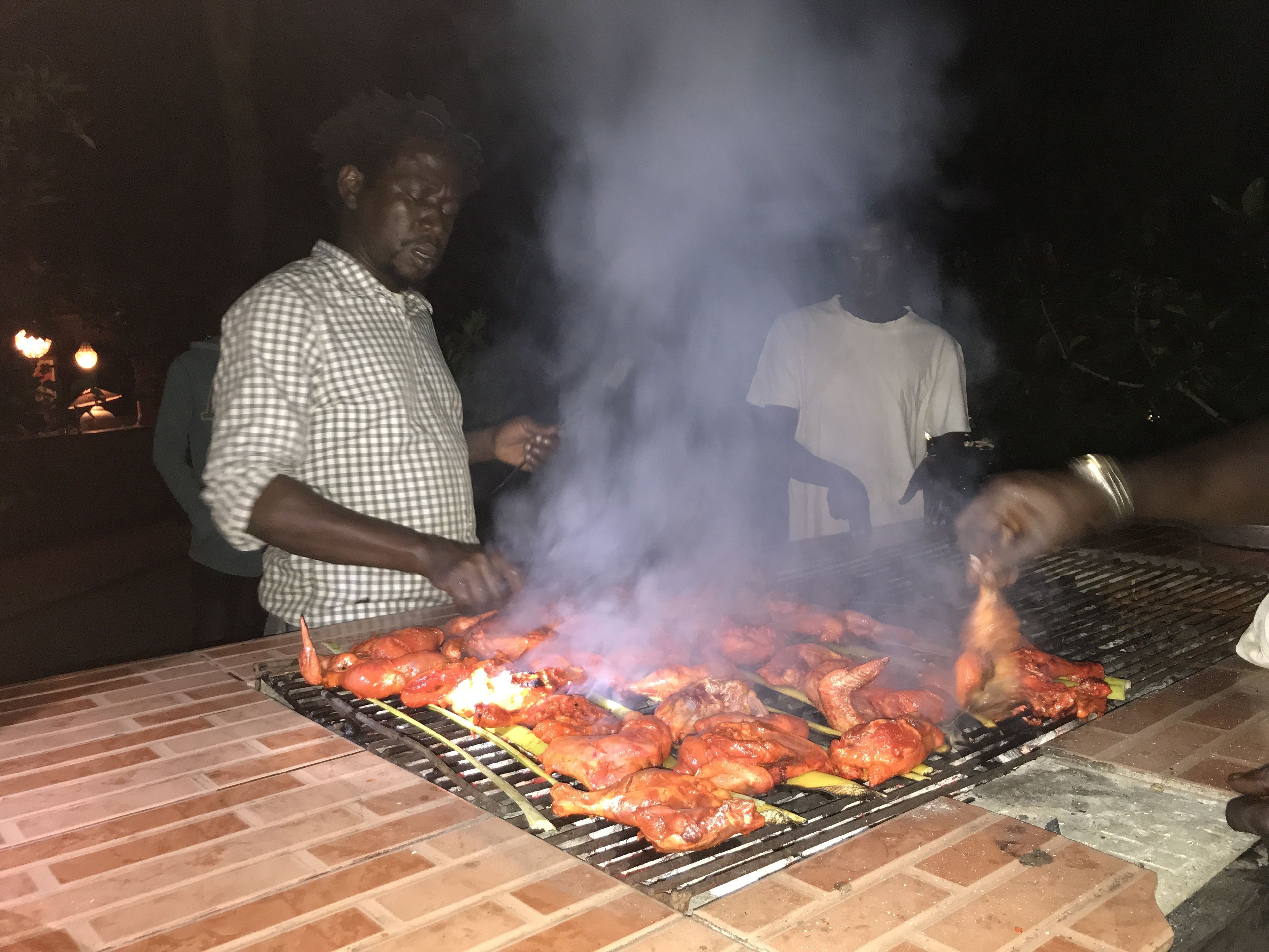 A grill with multiple skewers of meat, smoke rising from the grill, and people around it.