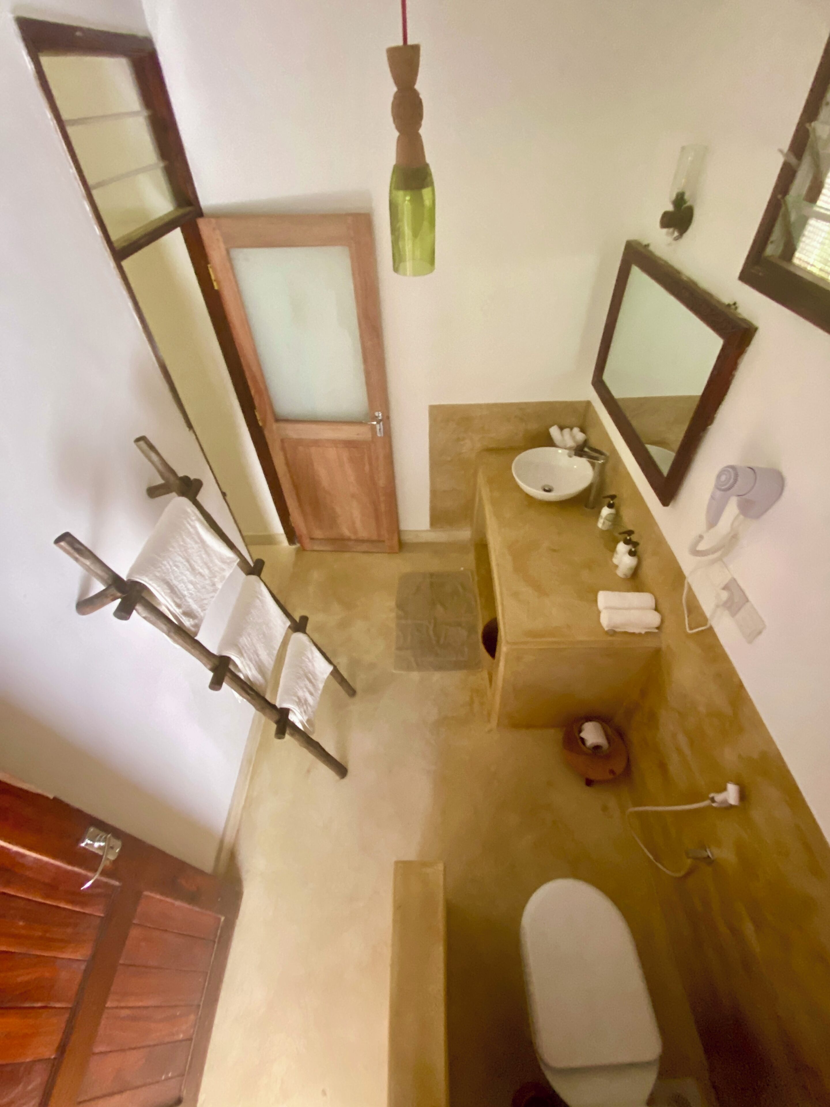 A bathroom with a wooden door, a sink, a toilet, a mirror, and a towel rack.