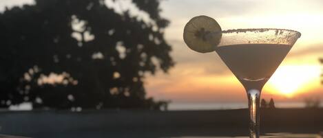 A martini glass with a lemon slice on a wooden surface, set against a sunset background.