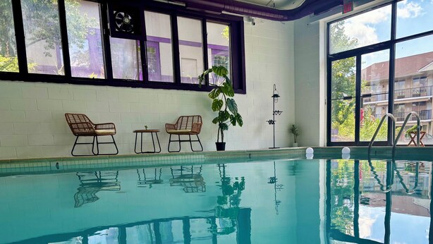 Une piscine intérieure à l’eau claire, entourée de fenêtres et de plantes en pot.