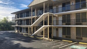 Un motel à plusieurs étages, doté d’un escalier central, d’un parking et offrant une vue sur un ciel dégagé.