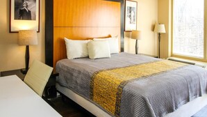 Une chambre d’hôtel avec un grand lit, deux tables de chevet, une chaise et une fenêtre avec des stores.