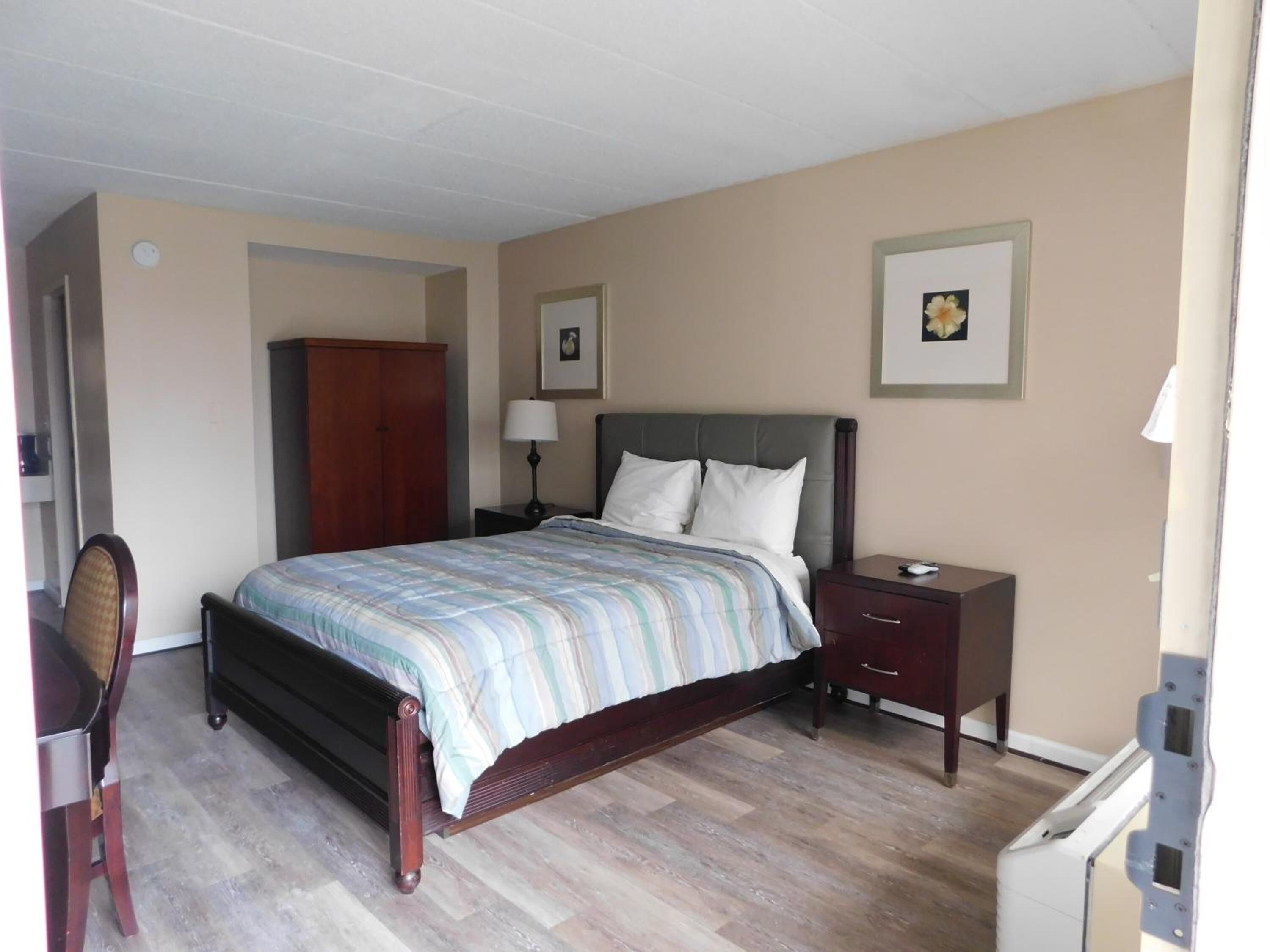 Um quarto com uma cama, mesa de cabeceira, escrivaninha e guarda-roupa.