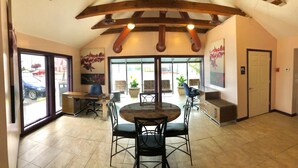 Une pièce spacieuse avec un plafond haut, une table à manger ronde entourée de chaises, une grande fenêtre donnant sur l’extérieur et une porte située sur le côté droit.