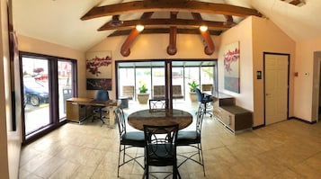 Una habitación amplia con techo alto, una mesa redonda de comedor con sillas, un ventanal con vistas al exterior y una puerta a la derecha.