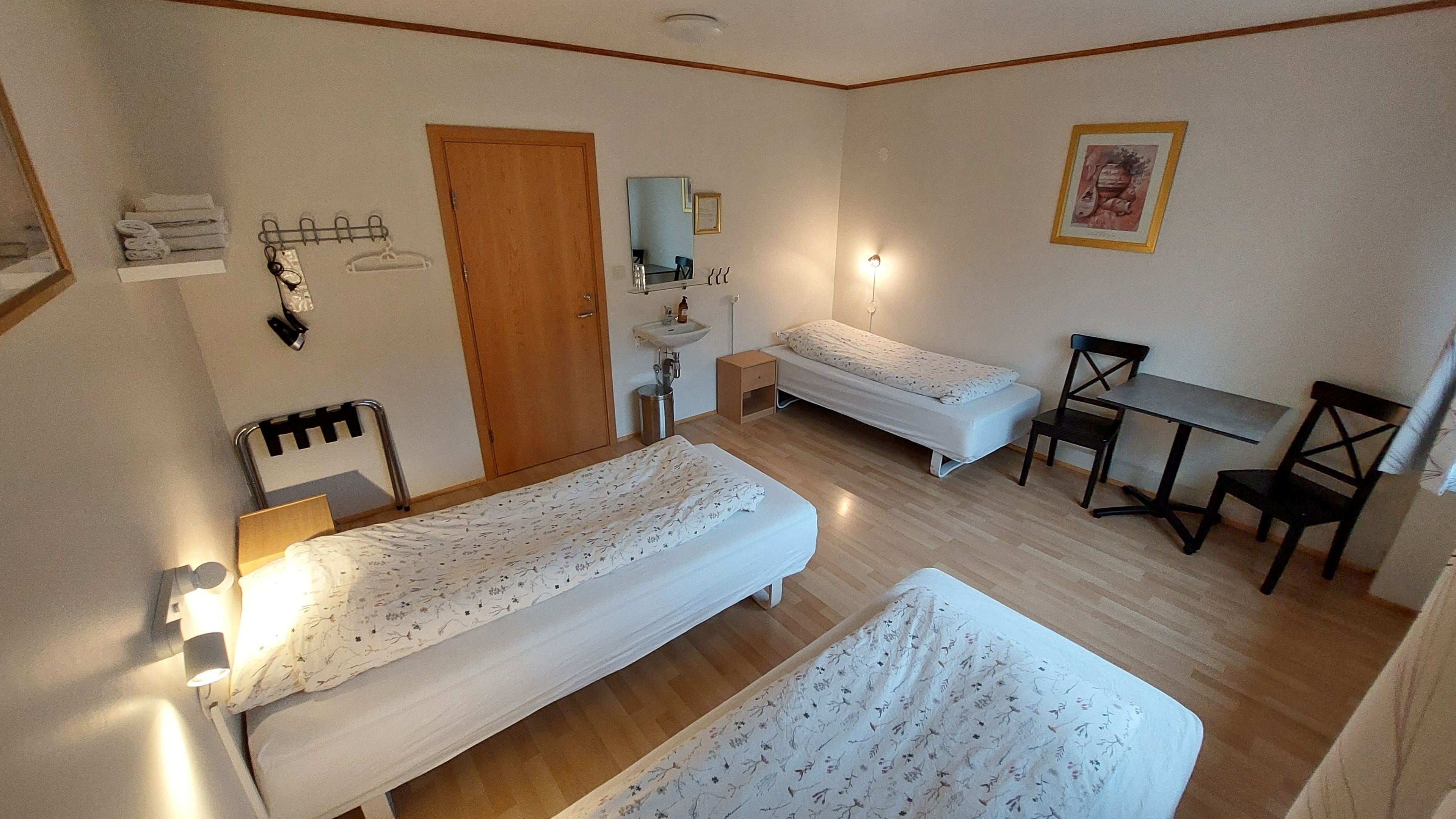 A room with two single beds, a small desk, a chair, a sink, and a door.