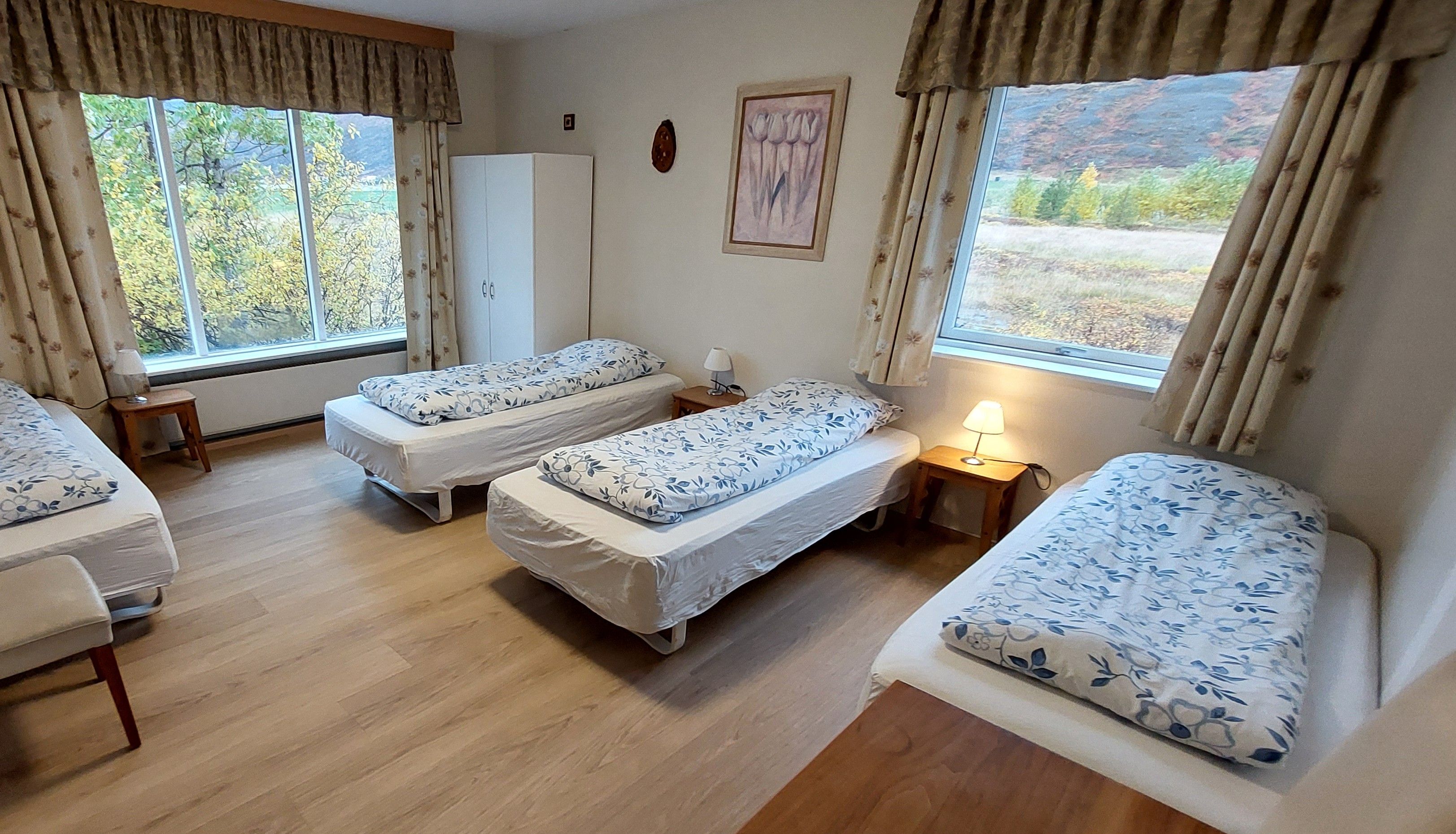 A room with three single beds, a wardrobe, and a painting on the wall.