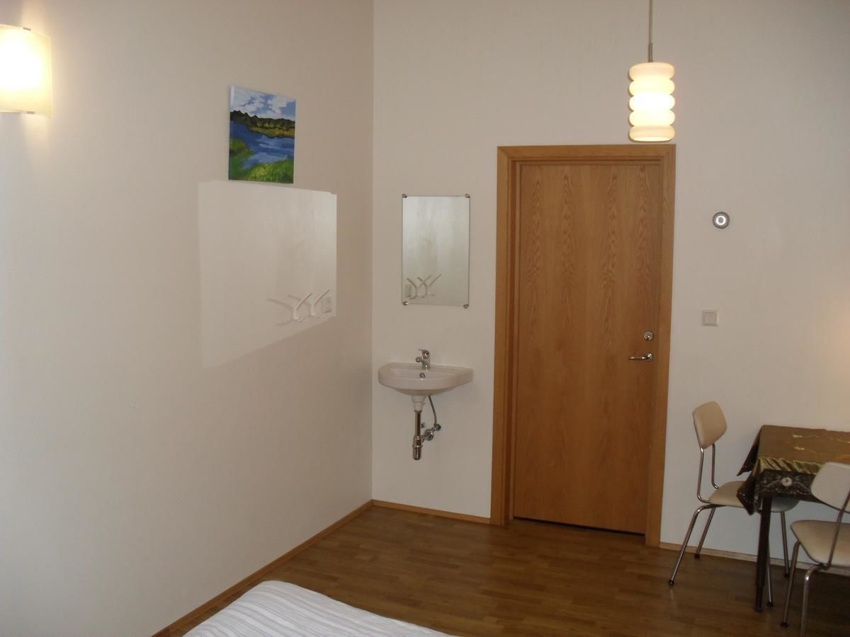 Una habitación pequeña y limpia con una puerta de madera, un lavamanos blanco, un espejo, un cuadro en la pared y una mesa con sillas.