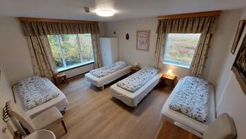 Una habitación con tres camas individuales, un escritorio de madera, una silla y un ventanal con cortinas.