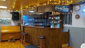 A bar area with wooden stools, a bar counter, and various bottles. - Kiðagil Guesthouse (Laugar)