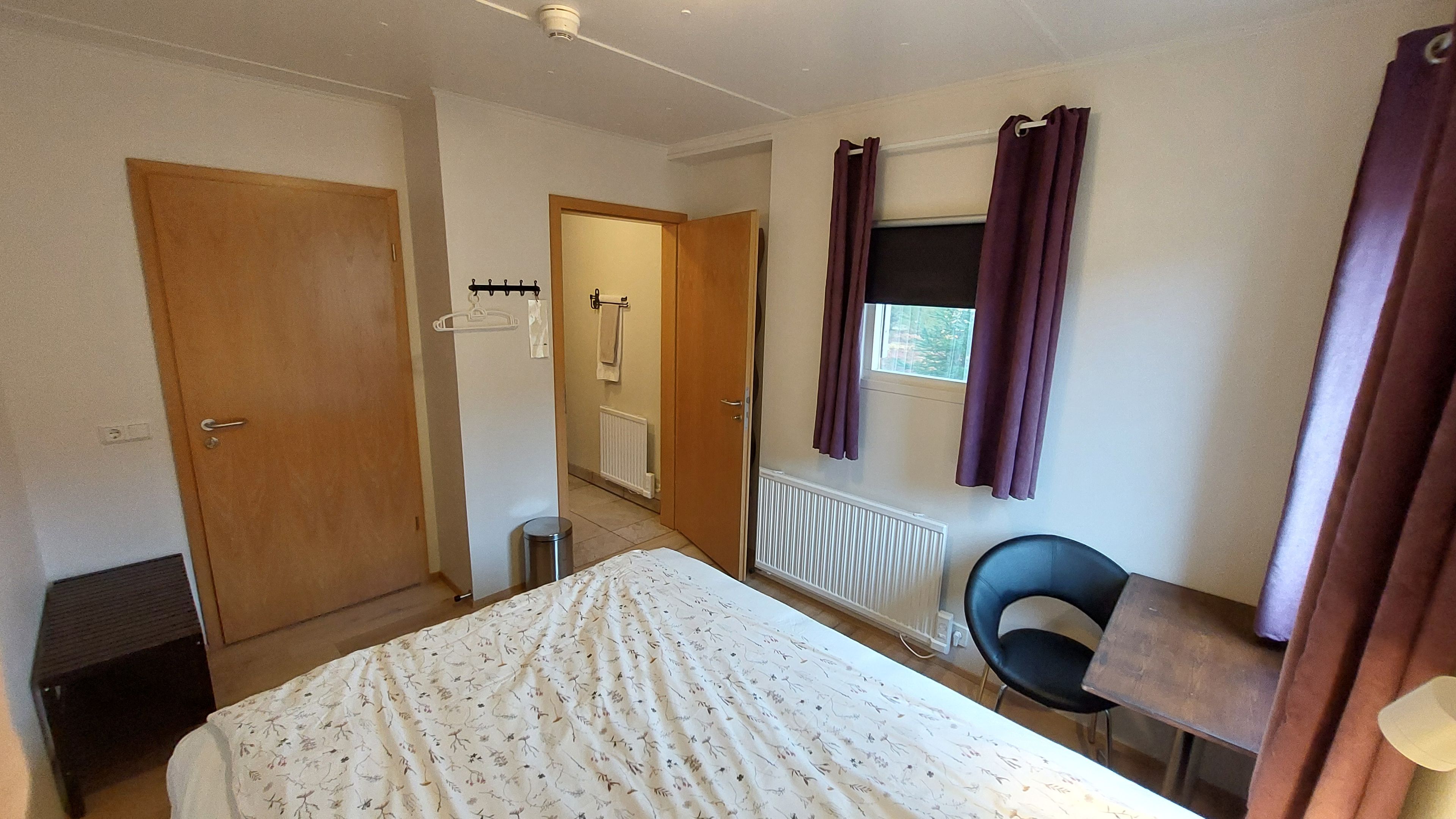 Une chambre d’hôtel avec un lit, une chaise, un bureau, un radiateur et une fenêtre avec des rideaux.