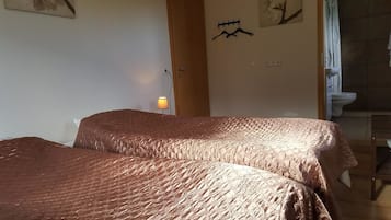 Una habitación con dos camas, una lámpara en la pared y un baño visible a través de una puerta abierta.