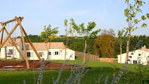 A white building with a tiled roof, surrounded by a well-maintained lawn and flowering plants.