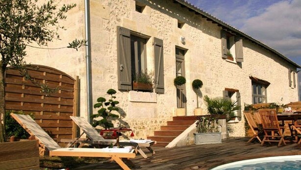 A stone building with a pool, wooden deck, and outdoor seating.