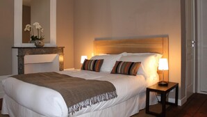 Una cama bien hecha con cabecera de madera, dos lámparas de noche y una mesita de noche con lámpara.