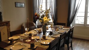 Comedor con una larga mesa dispuesta para una comida, destacando un florero con flores amarillas, una vela y diverso menaje de mesa.
