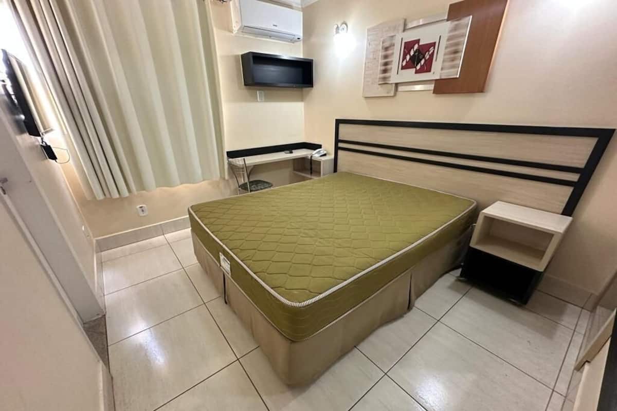 Une chambre à coucher comprenant un lit, un bureau, une chaise, un téléviseur et une étagère fixée au mur.