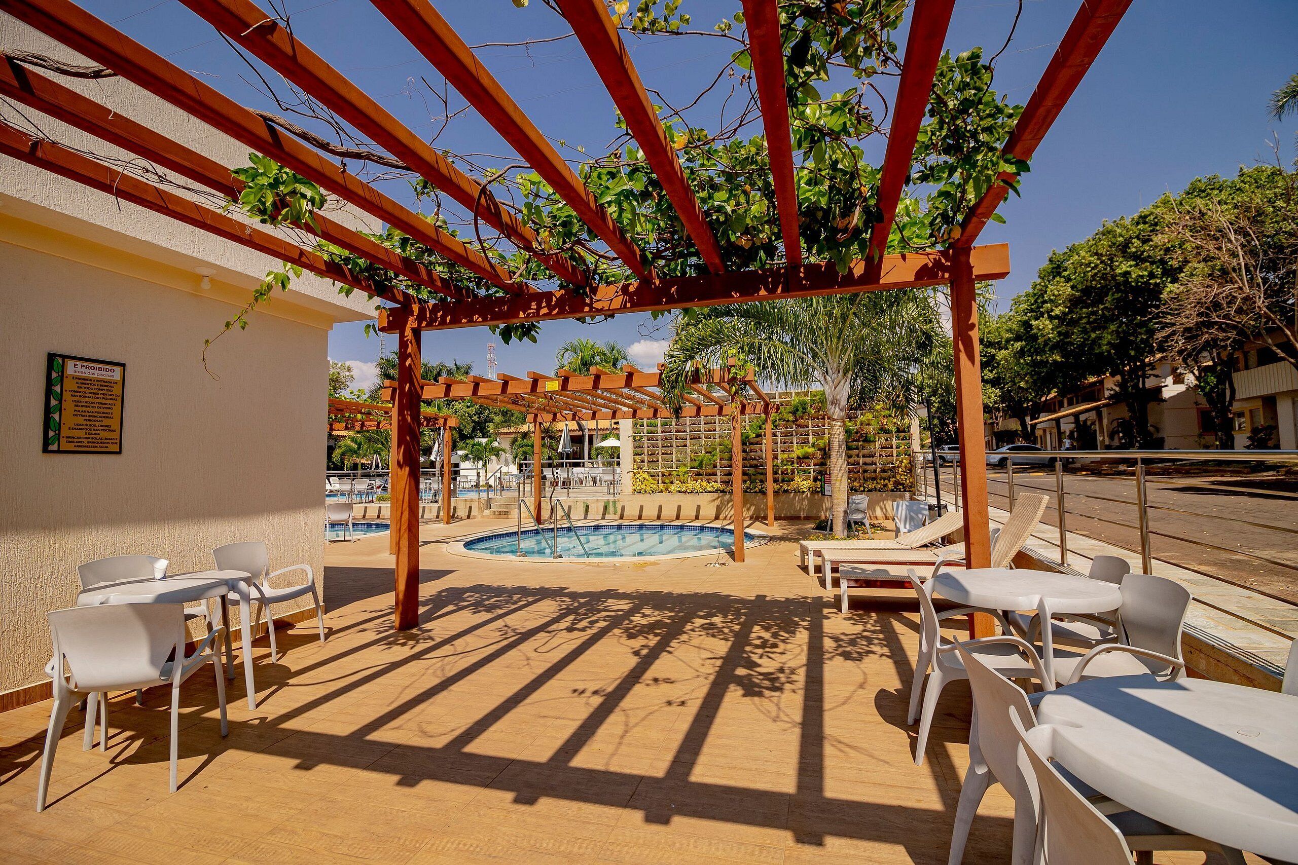 A poolside area with a pergola, white chairs, and tables.