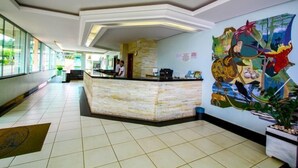 Un vestíbul d'hotel amb una recepció, un mural gran i un terra de rajoles.