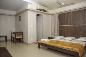 A bedroom with a bed, bedside table, chair, and a wardrobe. - Pai Resorts (Belagavi)