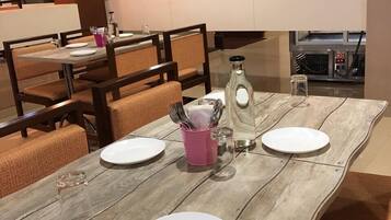 A dining area with a wooden table set for four, including plates, cutlery, and a pink cup.