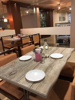 A dining area with a wooden table set for four, including plates, cutlery, and a pink cup. - Pai Resorts (Belagavi)
