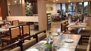 A restaurant with multiple dining tables, chairs, and a large window providing a view of the outdoors. - Pai Resorts (Belagavi)