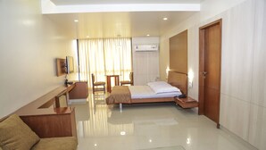 A hotel room with a bed, a desk, a chair, a sofa, and a television. - Pai Resorts (Belagavi)