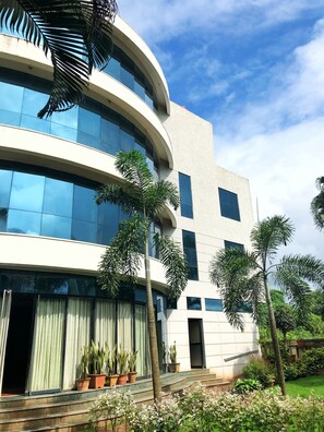 A modern building with large windows and a curved facade, surrounded by potted plants and a well-maintained lawn. - Pai Resorts (Belagavi)